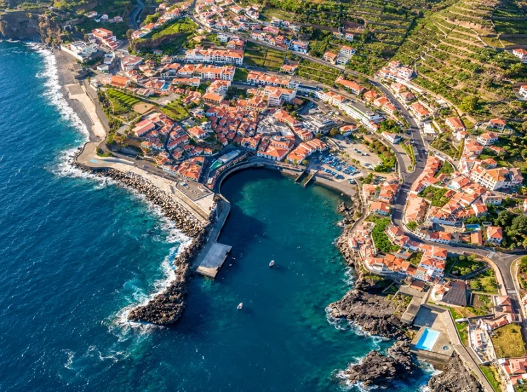Vista aérea da baía de Câmara de Lobos, rodeada por casas e encostas cultivadas.