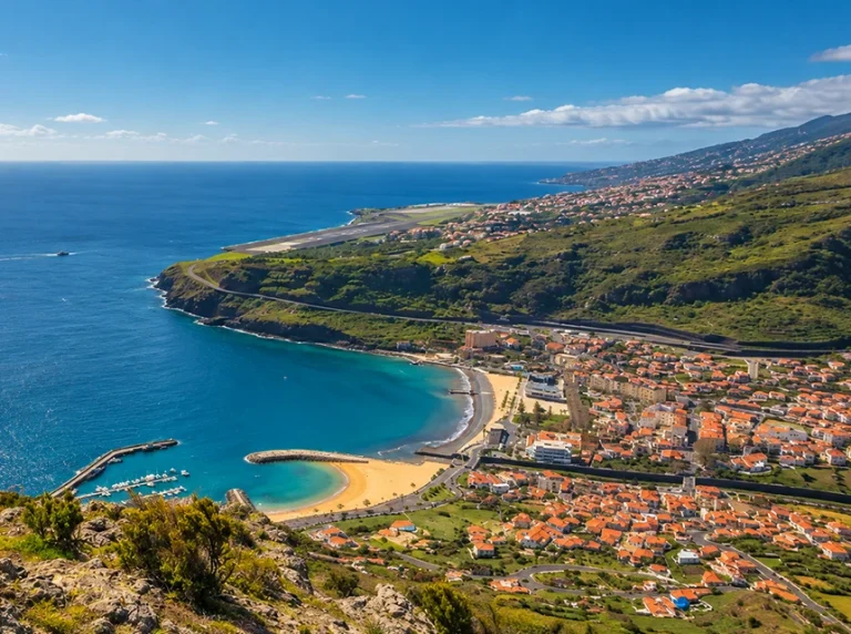 Vista panorâmica da baía de Machico, com a praia, o porto e as encostas verdes.