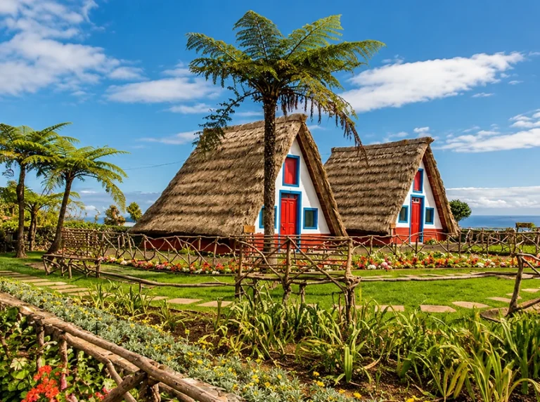 Casas tradicionais de Santana com telhados de colmo, rodeadas por um jardim.